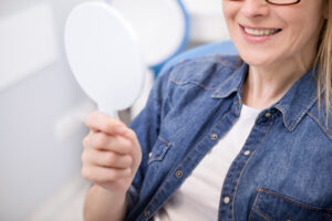 Female patient examining her teeth in the mirror after dental implant placement.