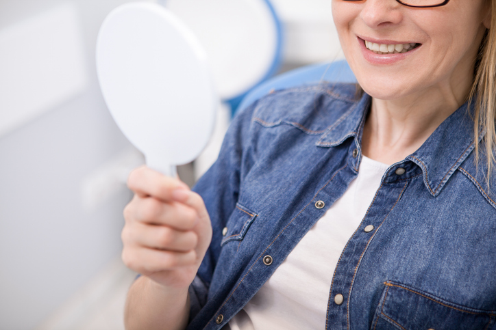 Female patient examining her teeth in the mirror after dental implant placement.